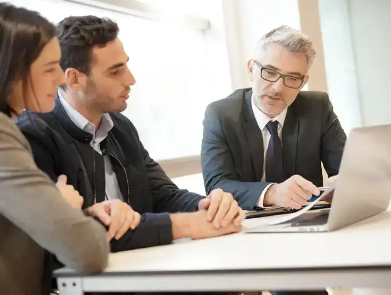 Financial advisor discussing self-employed mortgages with clients, laptop and paperwork visible.